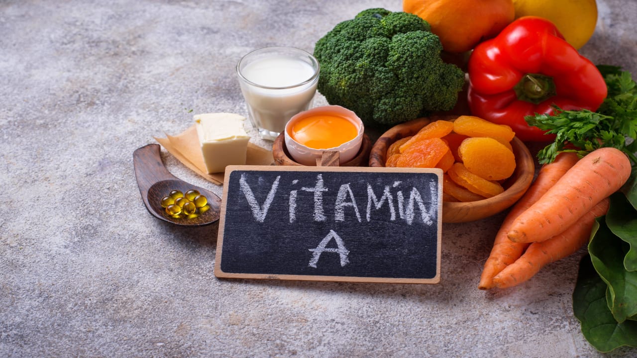 Sebze, mevye, bal, süt, kurukayısı bir arada duruyorlar ve önlerinde küçük bir karatahta üzerinde teşebir ile yazılmış Vitamin A yazısı duruyor.