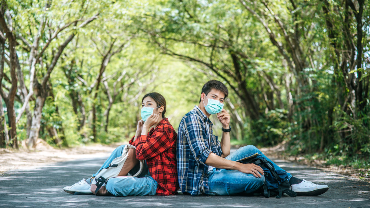 Yüzlerinde medikal yüz maskesi takan ve yol kenarında birbirine sırtını dayamış şekilde oturan çift
