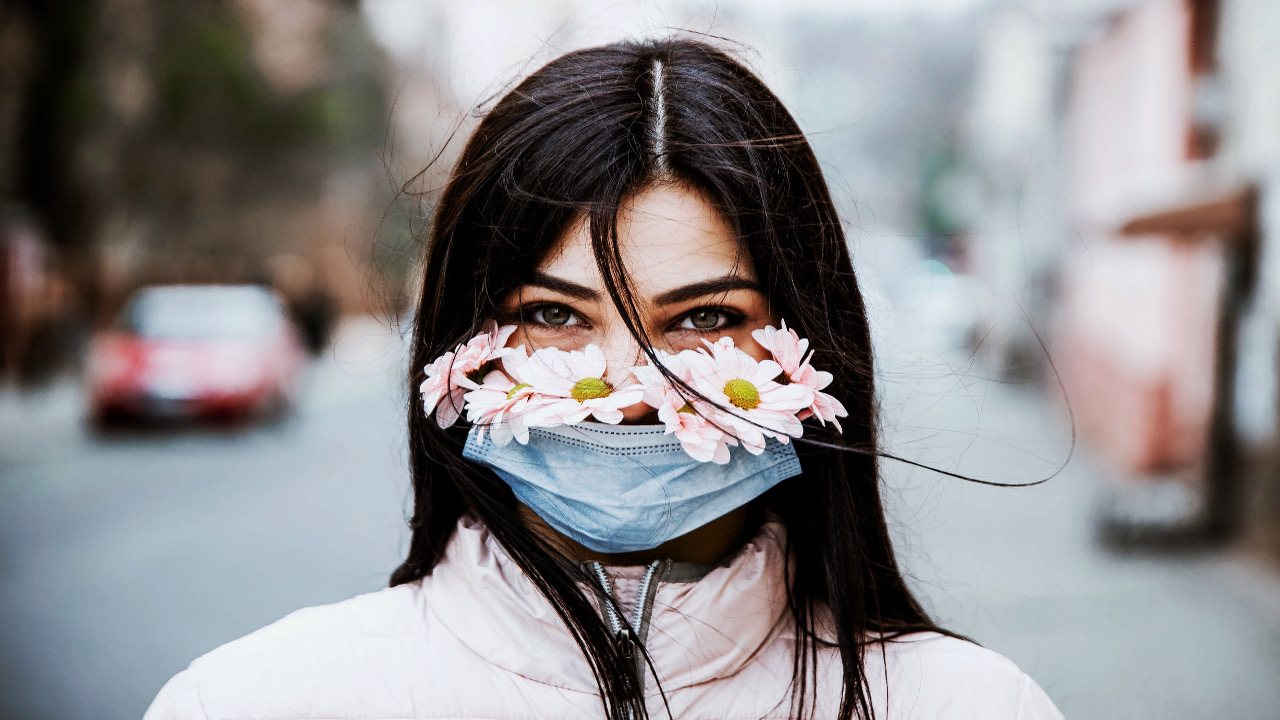 Bir kadın, sokakta çiçek bulunan yüz maskesi takmış şekilde görülmektedir.