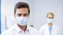 Bir erkek ve bir kadın doktor yüzlerinde cerrahi maske ile duruyor